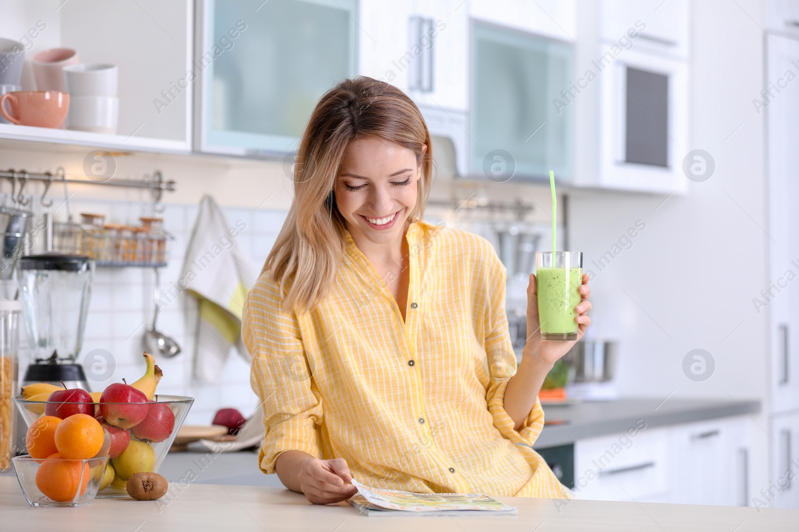 Photo of Young woman with glass of tasty healthy smoothie at table in kitchen