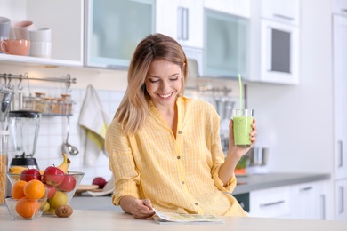 Young woman with glass of tasty healthy smoothie at table in kitchen