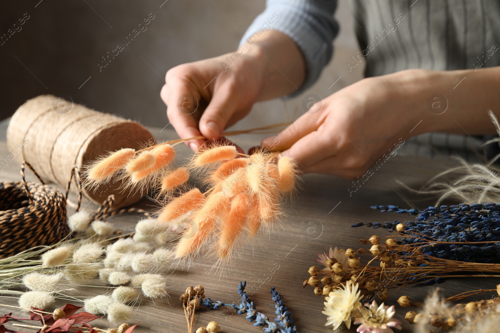 Photo of Florist making bouquet of dried flowers at wooden table, closeup