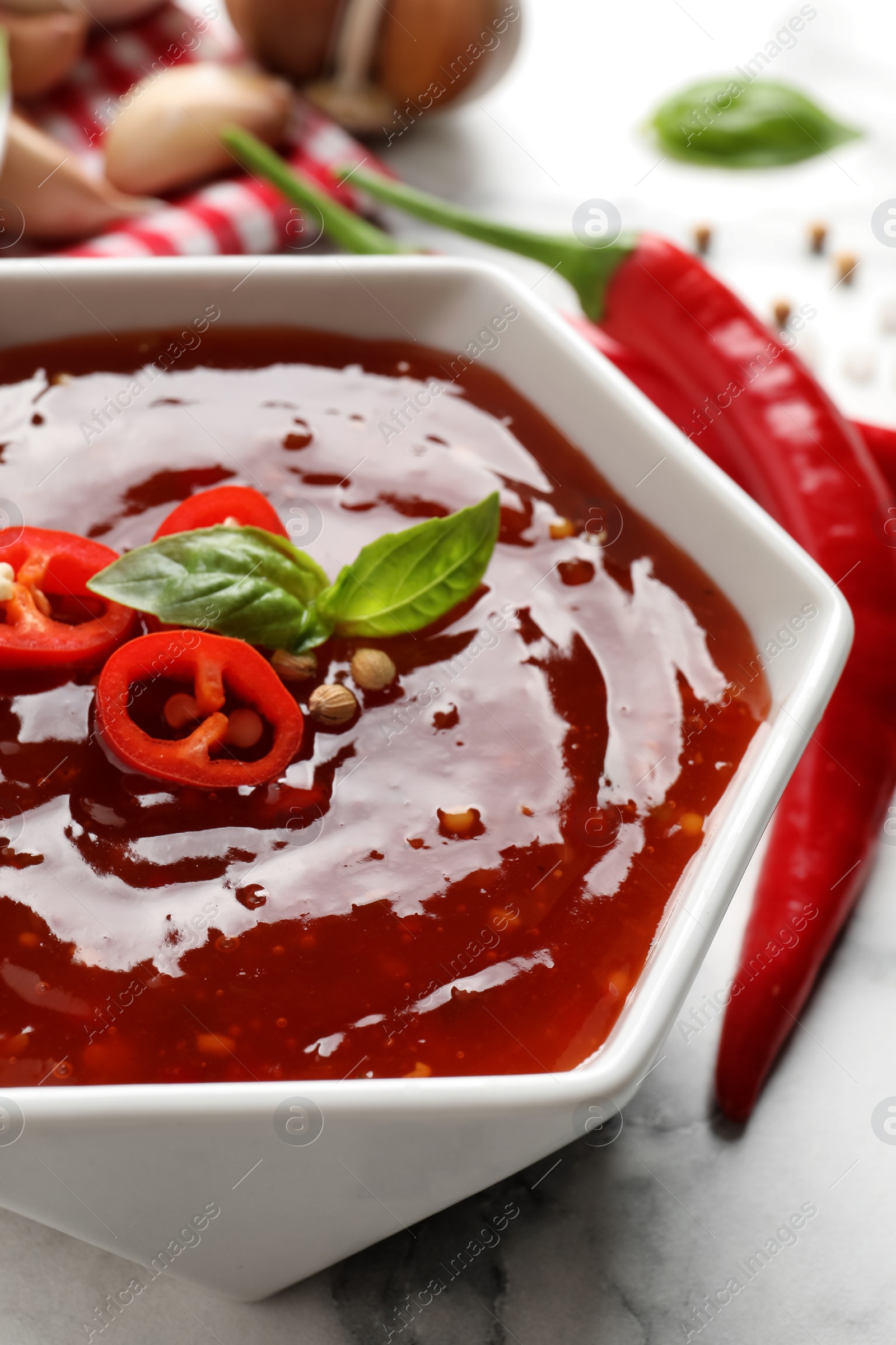 Photo of Spicy chili sauce with basil in bowl on table, closeup