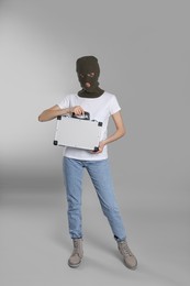 Woman wearing knitted balaclava with metal briefcase on grey background