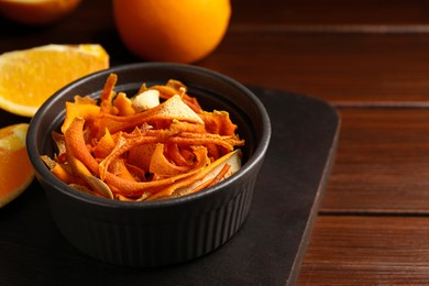 Bowl with dry orange peels and fresh fruits on wooden table, closeup