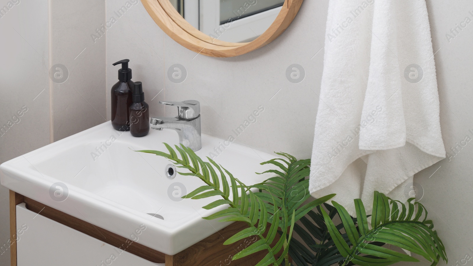 Photo of Hanging towel, sink, houseplant and toiletries in bathroom. Interior design