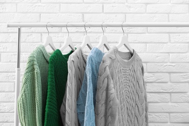 Collection of warm sweaters hanging on rack near brick wall