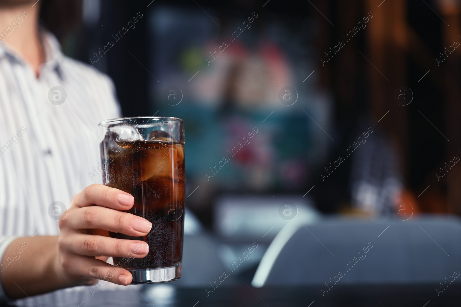 Photo of Woman with glass of refreshing cola at table indoors, closeup. Space for text