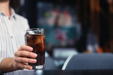 Photo of Woman with glass of refreshing cola at table indoors, closeup. Space for text