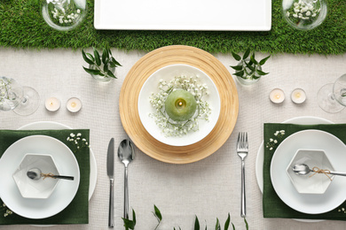 Elegant table setting with green plants on light cloth, flat lay