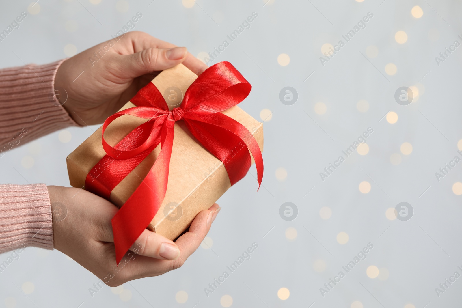 Photo of Woman holding gift box with red bow against blurred festive lights, closeup and space for text. Bokeh effect