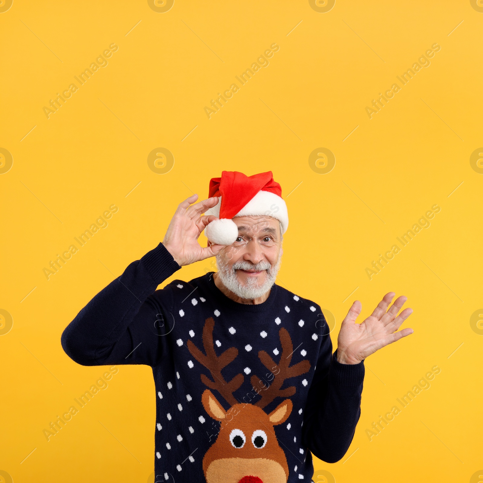 Photo of Senior man in Christmas sweater and Santa hat on orange background