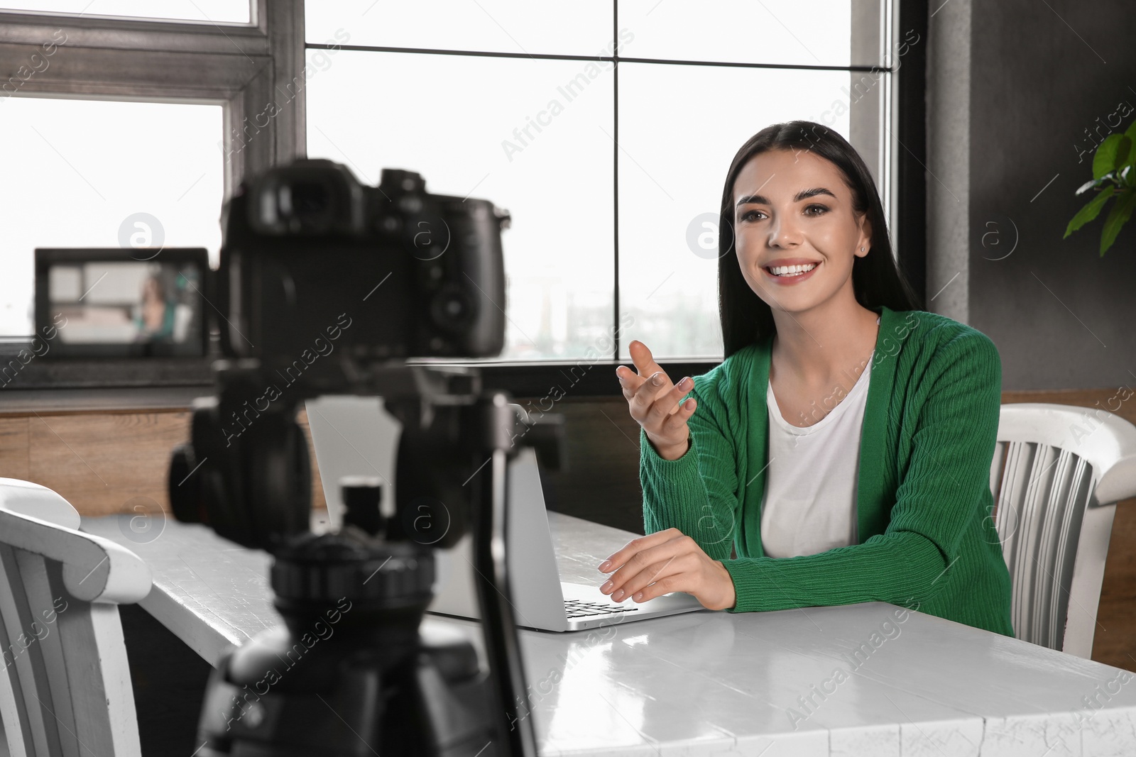 Photo of Young blogger with laptop recording video on camera at cafe