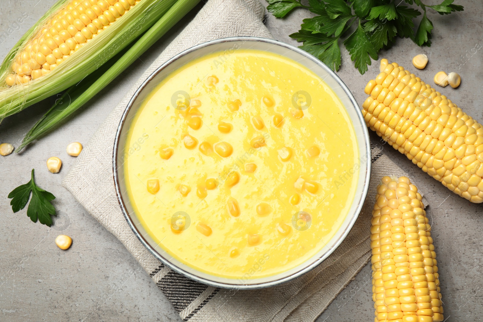 Photo of Delicious creamy corn soup and cobs on grey table, flat lay