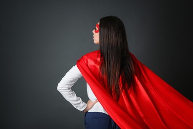 Photo of Confident businesswoman wearing superhero cape and mask on grey background, back view