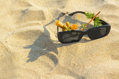 Stylish sunglasses and tropical flower on sand. Space for text