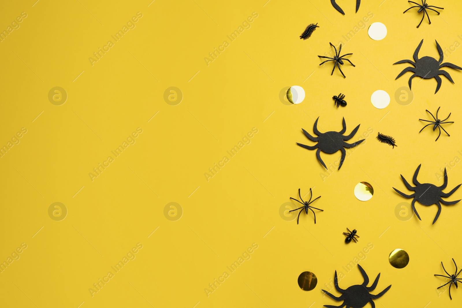 Photo of Flat lay composition with spiders and golden confetti on pale yellow background, space for text. Halloween celebration