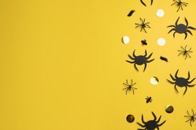 Photo of Flat lay composition with spiders and golden confetti on pale yellow background, space for text. Halloween celebration