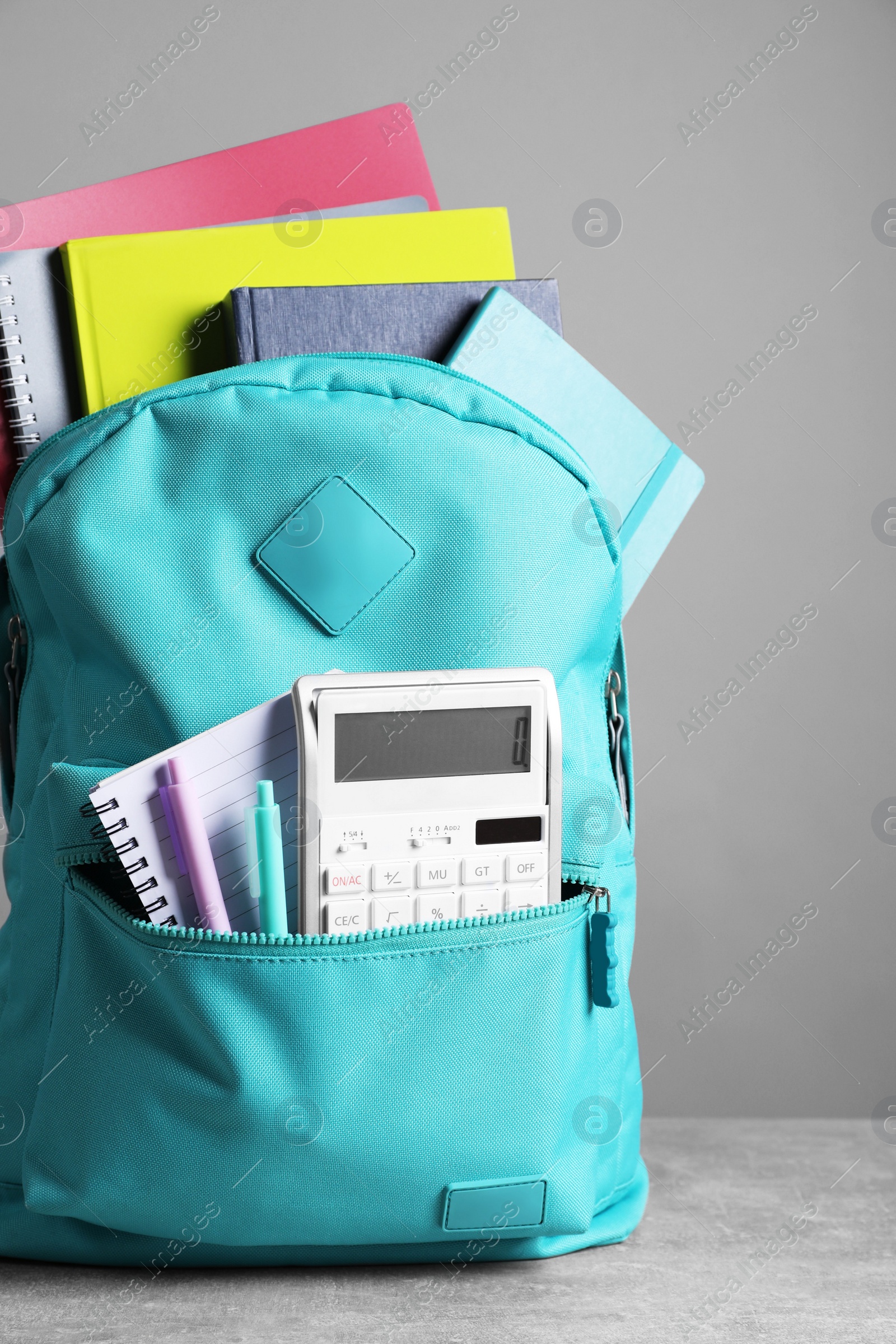 Photo of Turquoise backpack and different school stationery on table against grey background