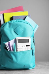 Turquoise backpack and different school stationery on table against grey background
