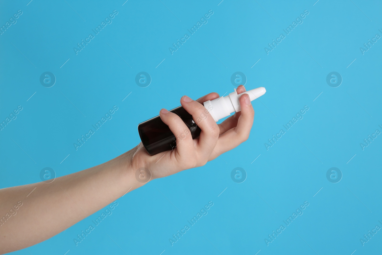 Photo of Woman holding nasal spray on light blue background, closeup