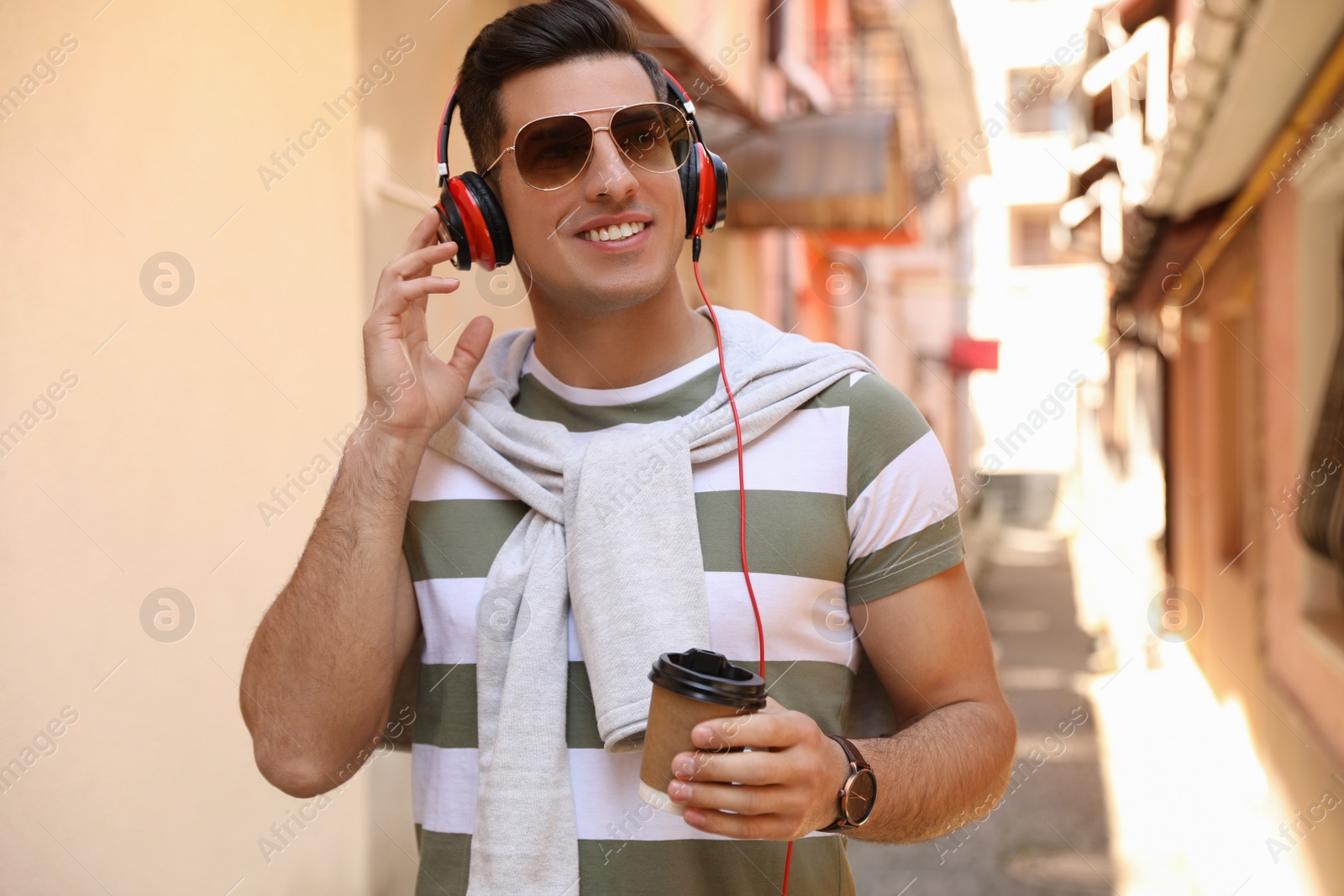 Photo of Happy man with coffee and headphones listening to music on city street