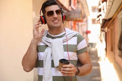 Happy man with coffee and headphones listening to music on city street
