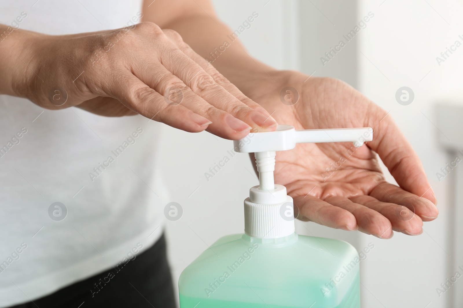 Photo of Woman applying antiseptic gel on hand indoors, closeup