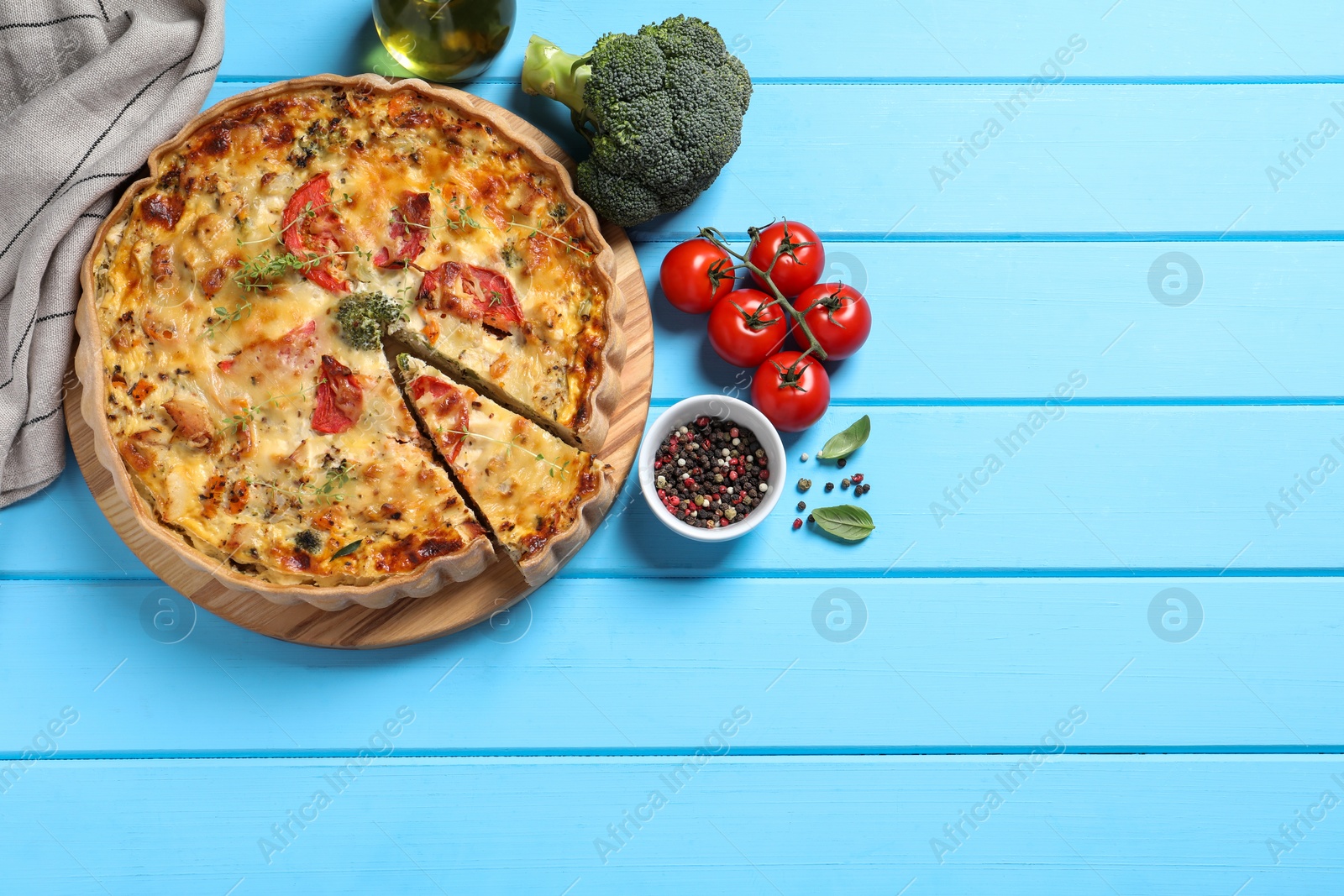 Photo of Tasty quiche with tomatoes and cheese served on light blue wooden table, flat lay. Space for text