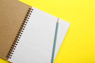 Photo of Notebook and pencil on yellow background, top view