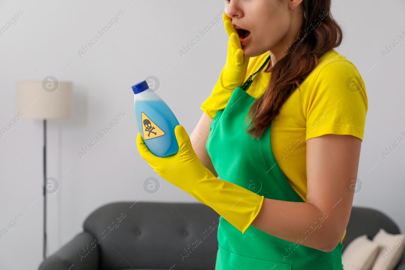 Photo of Woman looking at bottle of toxic household chemical with warning sign, closeup