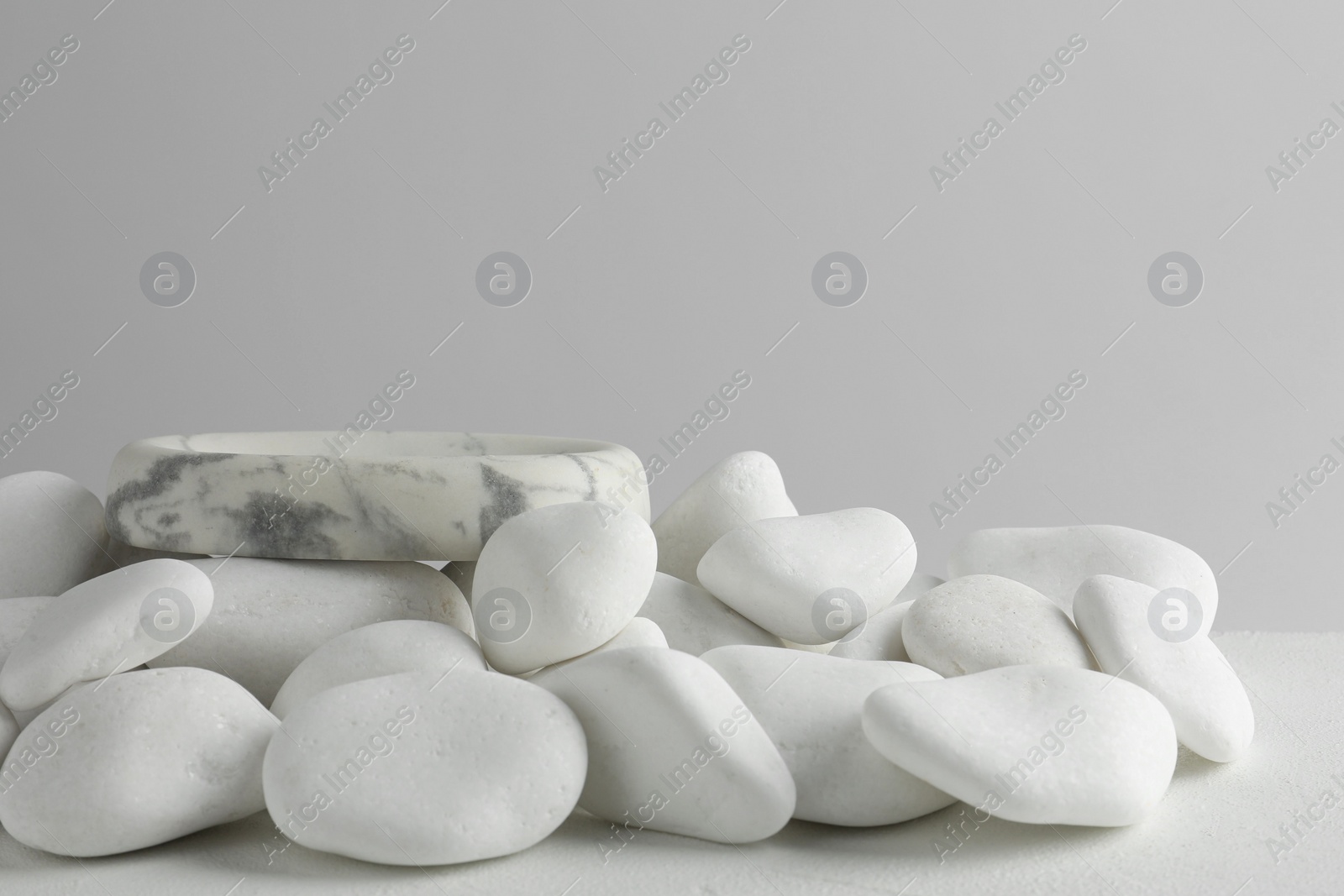 Photo of Presentation for product. Stone podium and white pebbles on table against light background. Space for text