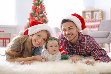 Photo of Happy couple with baby in Christmas hats at home