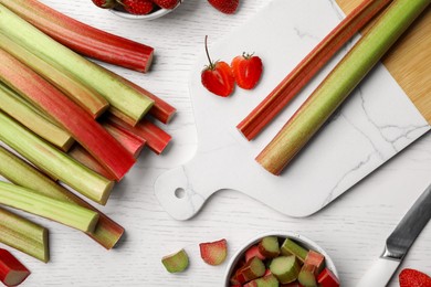 Photo of Fresh rhubarb stalks and strawberries on white wooden table, flat lay