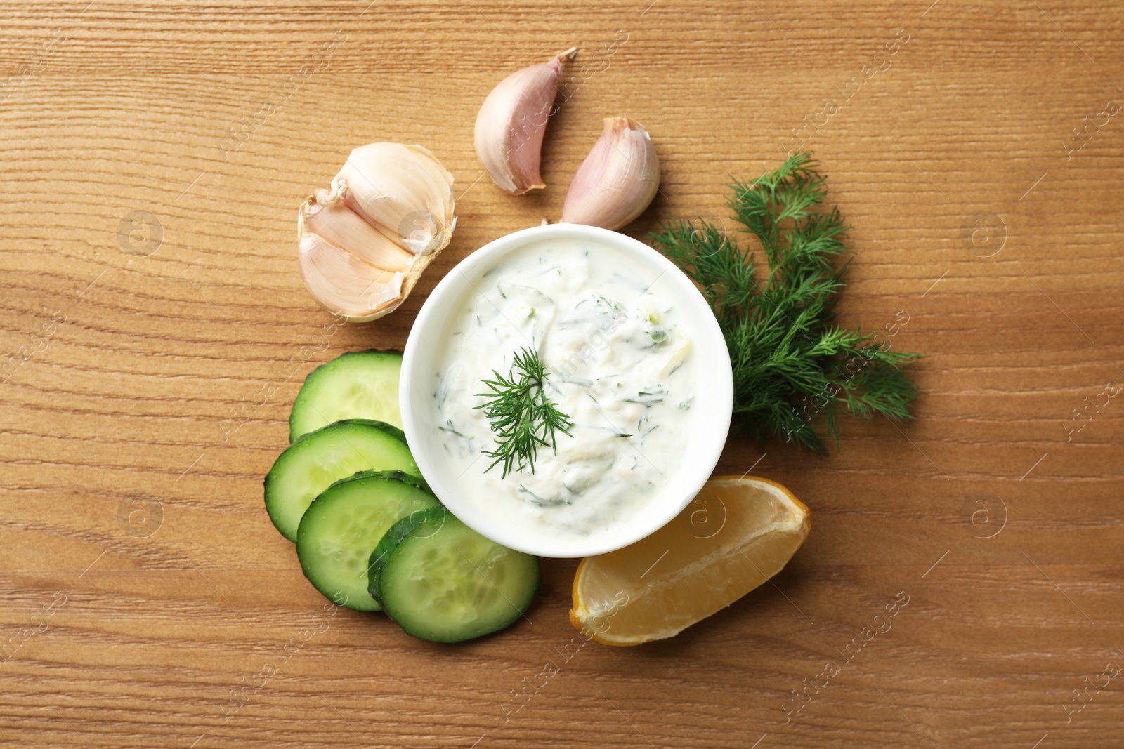 Photo of Cucumber sauce with ingredients on wooden background, flat lay. Traditional Tzatziki