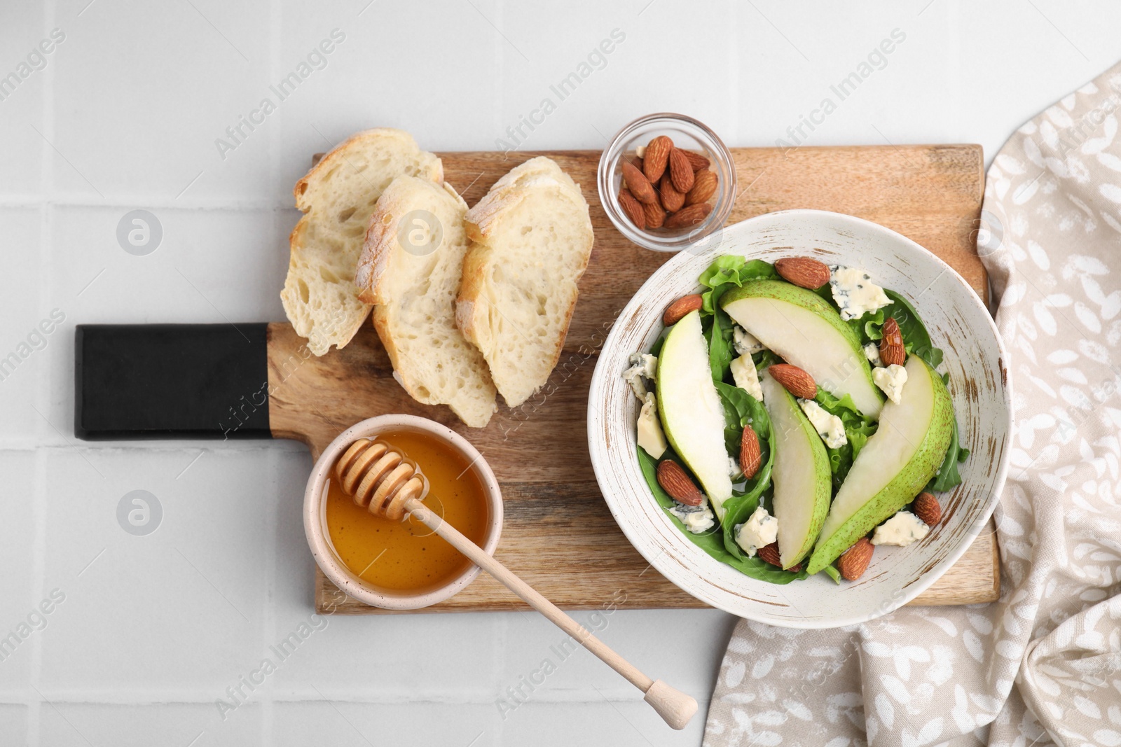 Photo of Delicious pear salad in bowl, honey and bread on light tiled table, top view