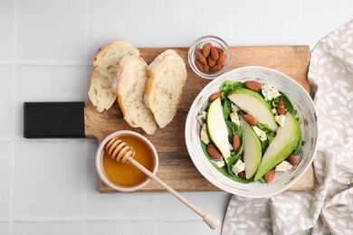 Photo of Delicious pear salad in bowl, honey and bread on light tiled table, top view