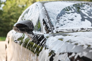Photo of Auto covered with cleaning foam at outdoor car wash, closeup