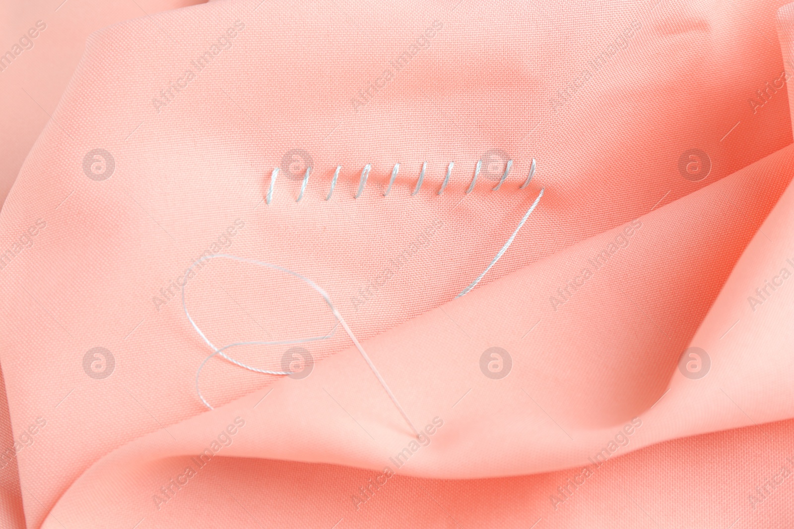 Photo of Sewing needle with thread and stitches on coral cloth, top view
