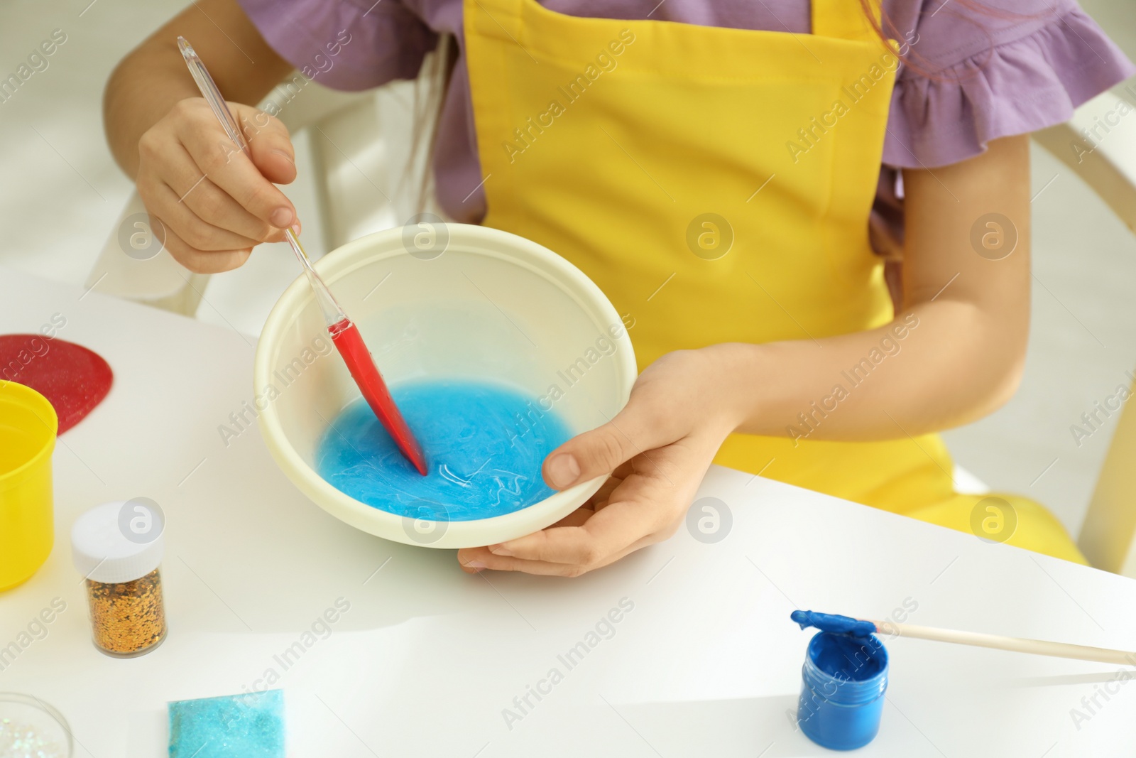 Photo of Little girl mixing ingredients with silicone spatula at table, closeup. DIY slime toy