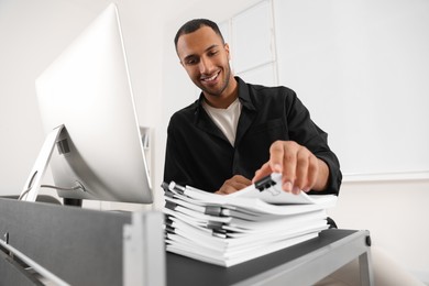 Photo of Happy man working with documents at grey table in office, low angle view