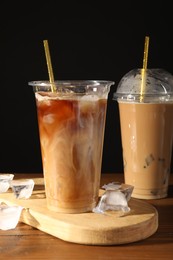 Photo of Refreshing iced coffee with milk in takeaway cups on wooden table against black background