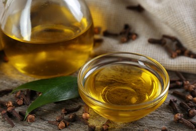 Photo of Essential oil and dried cloves on wooden table, closeup