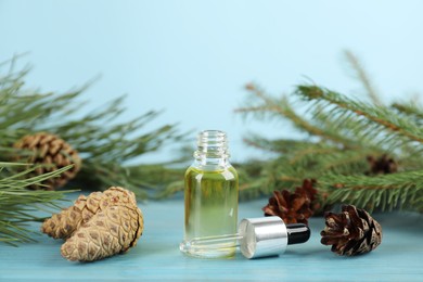 Photo of Pine essential oil, cones and branches on light blue wooden table