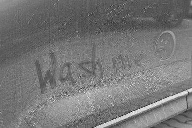 Phrase Wash Me and sad emoticon drawn on dirty car, closeup