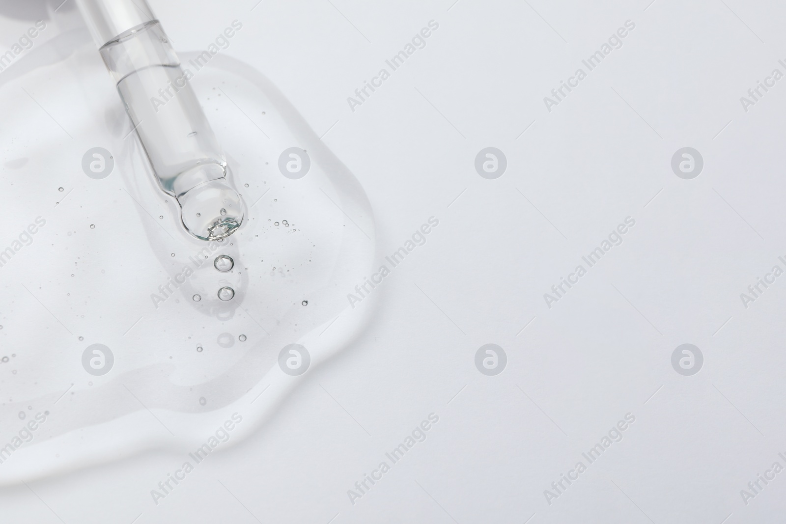 Photo of Dripping cosmetic oil from pipette onto light surface, closeup. Space for text