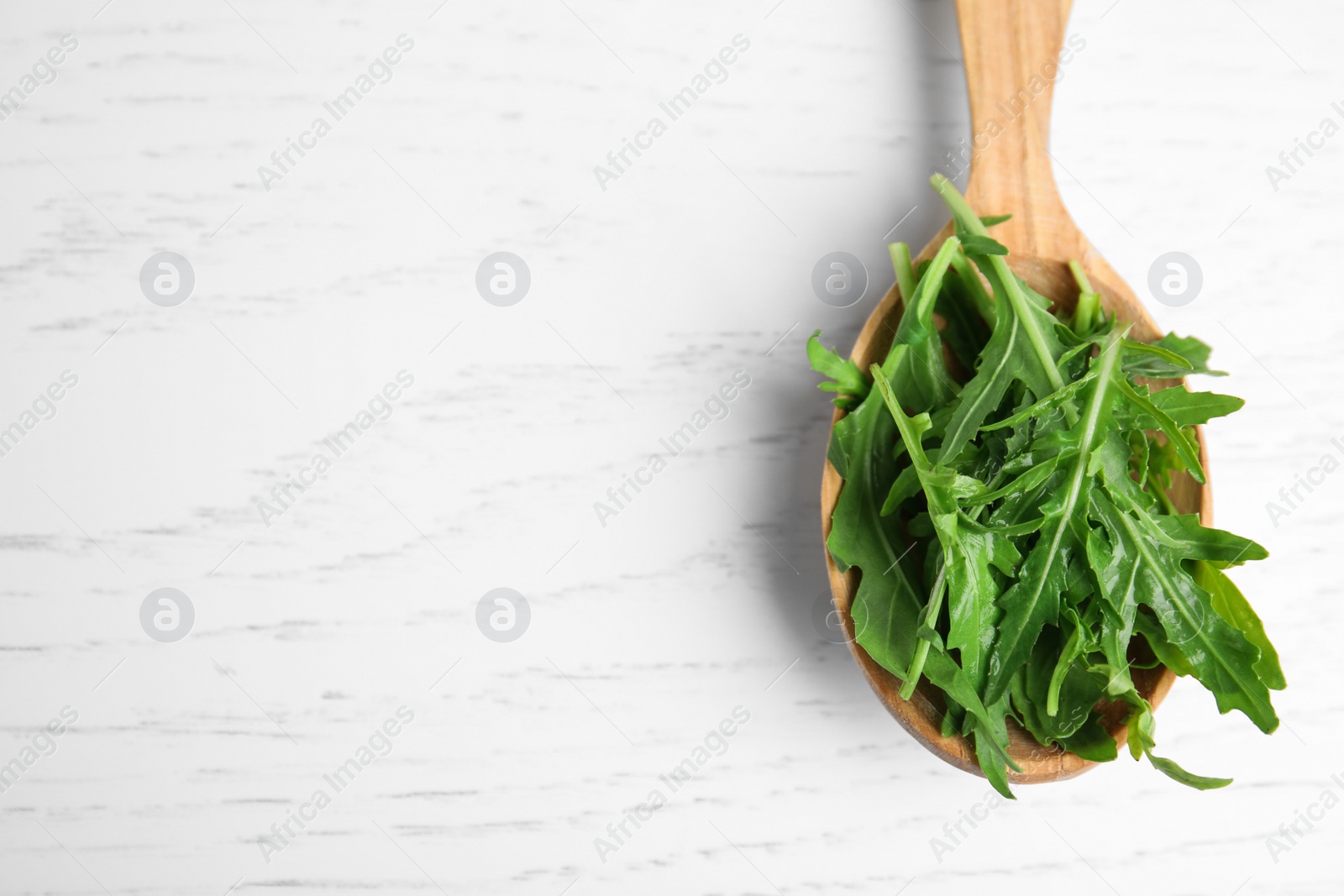 Photo of Fresh arugula in spoon on white wooden table, top view. Space for text