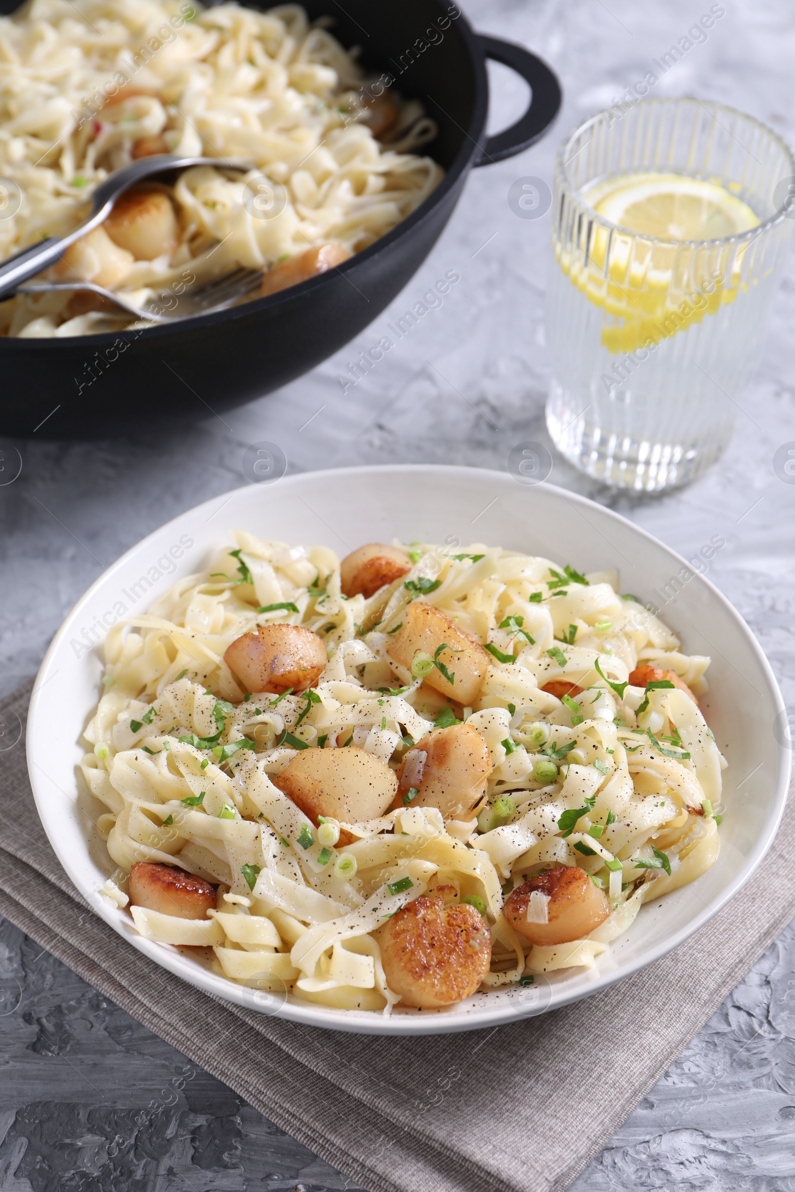 Photo of Delicious scallop pasta with spices served on gray textured table, closeup