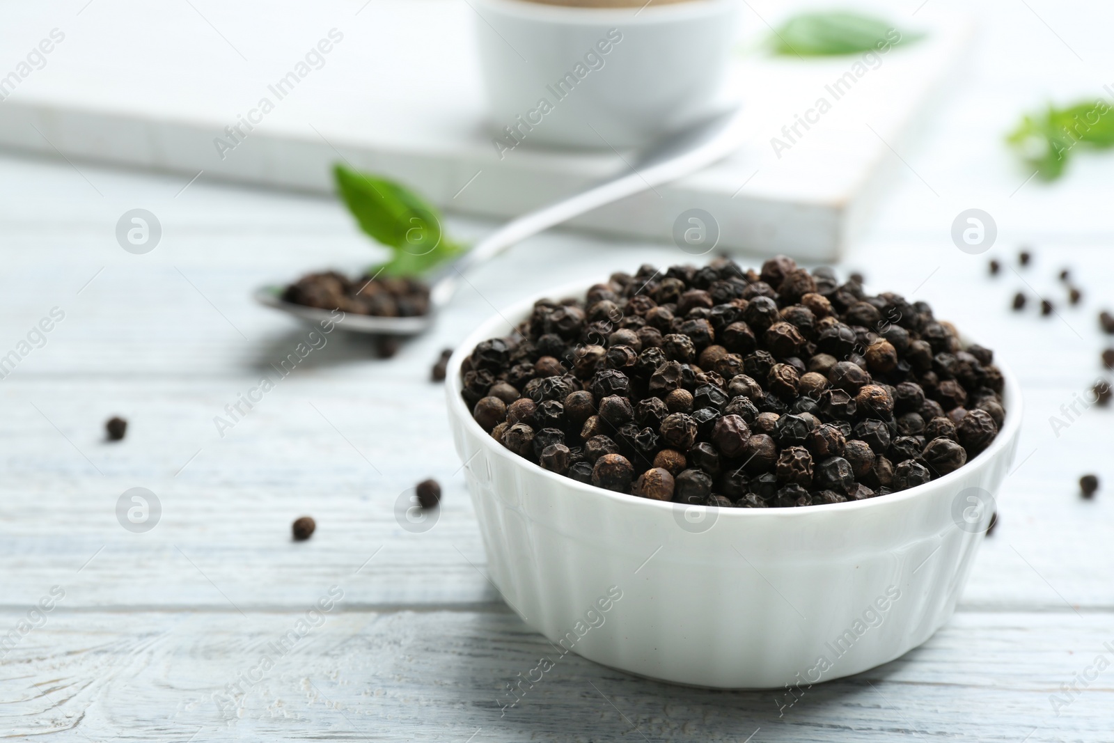 Photo of Bowl of black pepper corns on white wooden table, space for text