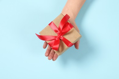 Woman holding gift box on light blue background, top view