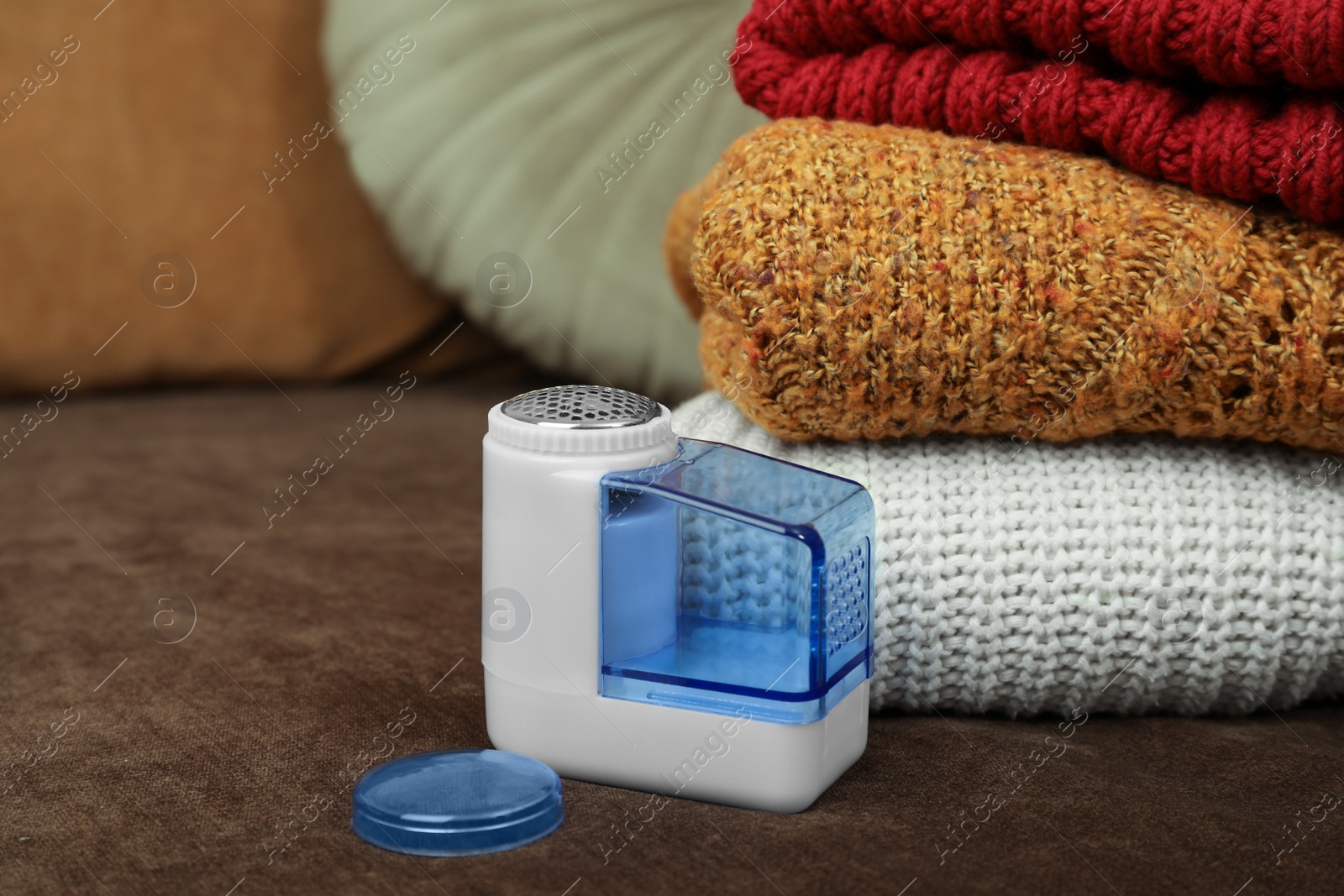 Photo of Modern fabric shaver and knitted clothes on sofa, closeup. Space for text