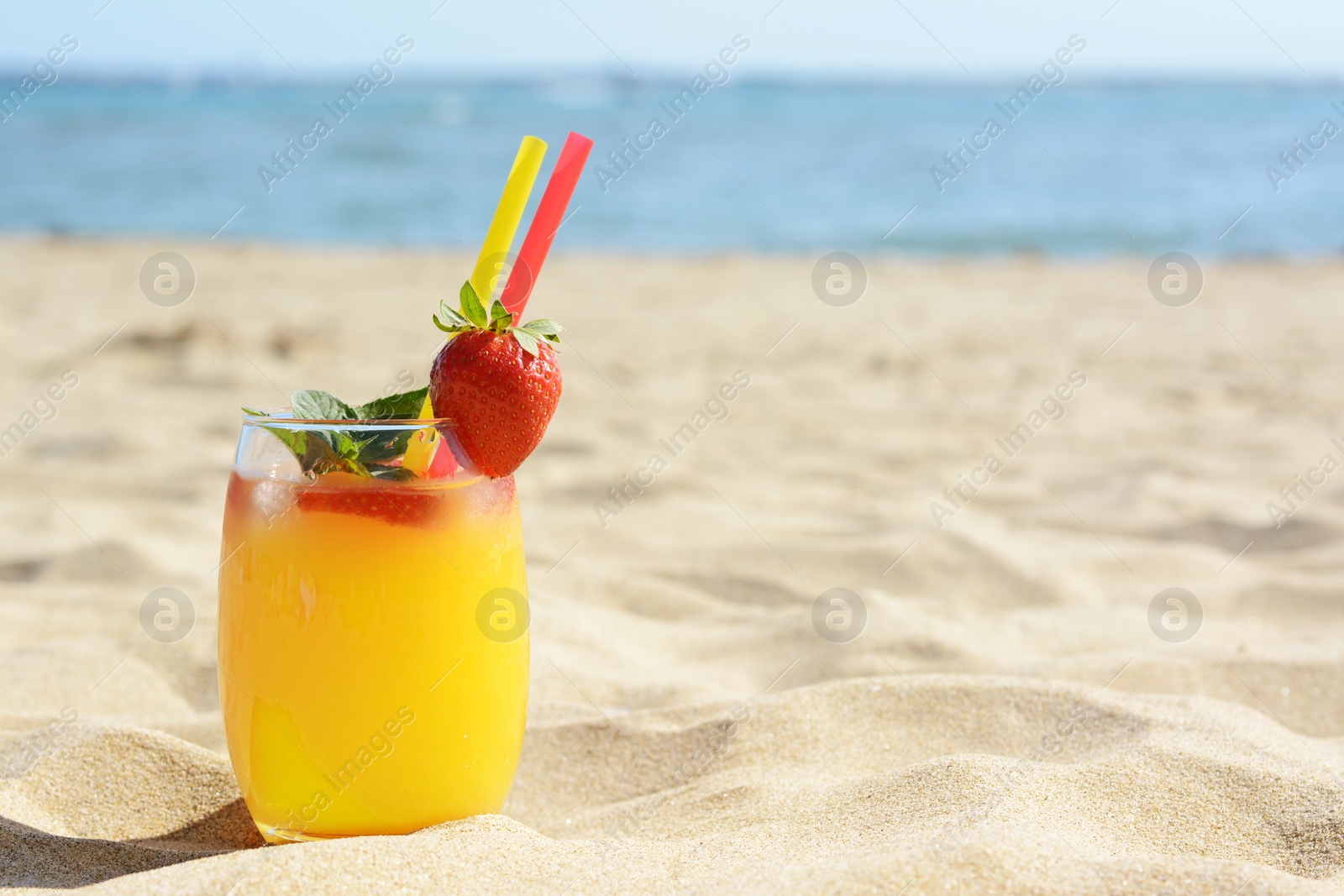 Photo of Glass of refreshing drink with strawberry on sandy beach near sea, space for text