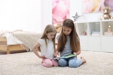 Cute little sisters reading book together at home